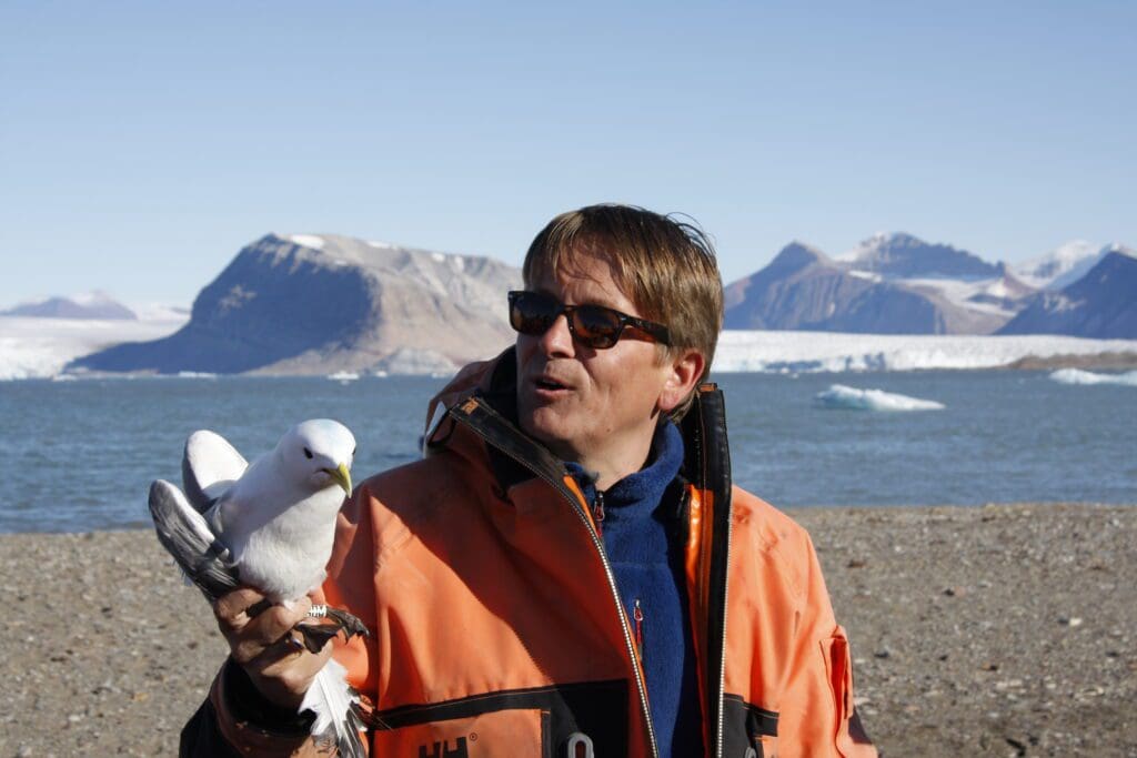 With a kittiwake in his hand and Kongsfjorden at his back, Geir Wing Gabrielsen is in his element. Photo: Eva Therese Jenssen / University Centre in Svalbard.
