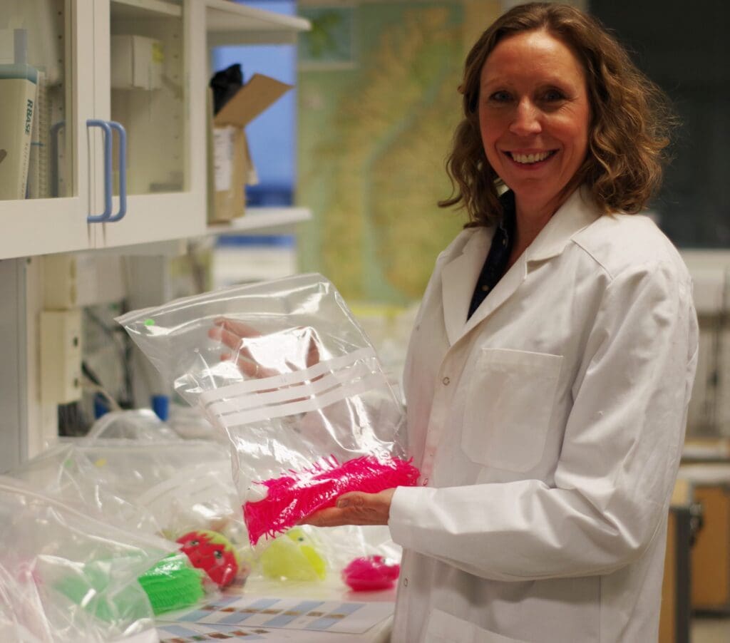 Foto av Pernilla som står i laboratoriet og smiler til kamera